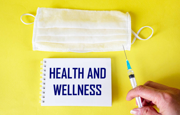 Zdrowie i wellness - koncepcja zdrowego stylu życia - tekst na notatniku. Lekarz trzymający strzykawkę, obok maski na żółtym tle - Zdjęcie, obraz