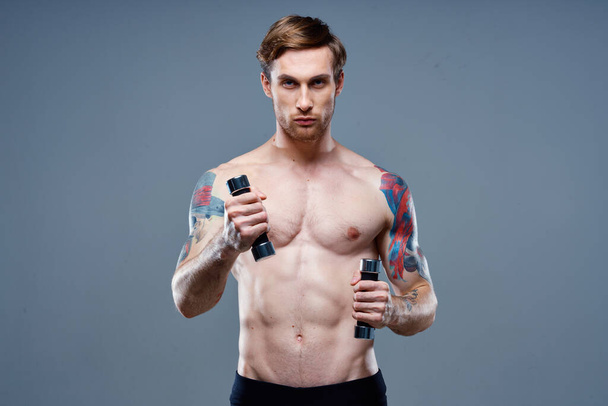 meztelen férfi csinál sport szürke háttér és súlyzó tetoválás vágott nézet - Fotó, kép