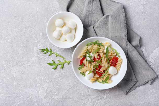 Top view of tasty vegetarian pasta with cherry tomatoes, soft cheese mozzarella and green arugula leaves on grey concrete background - Photo, image