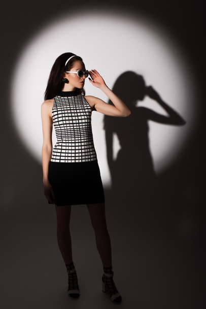 full length of lighting on trendy model adjusting sunglasses and posing on grey  - Фото, изображение