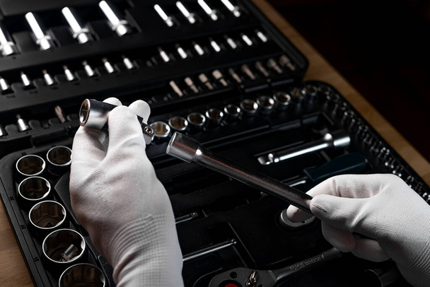 Repairman hands closeup in white gloves holding metal handle extension tool over dark background with toolbox, case - Fotó, kép