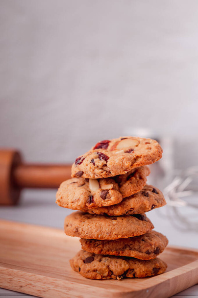 Piles of delicious chocolate chip cookies on a white plate with a milk bottle. Pastry utensils with white linen napkins on a wooden table. Delicious on a white plate with a bottle of milk. - Foto, Imagem