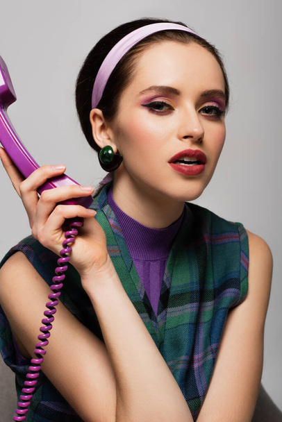 brunette young woman holding purple retro phone isolated on grey - Fotoğraf, Görsel