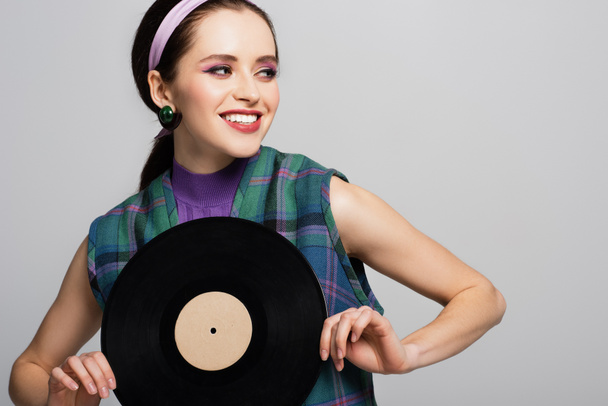 smiling woman in headband holding vintage vinyl disc isolated on grey - Photo, Image