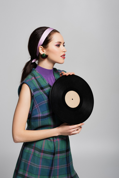 jong brunette vrouw in hoofdband houden retro vinyl disc geïsoleerd op grijs - Foto, afbeelding