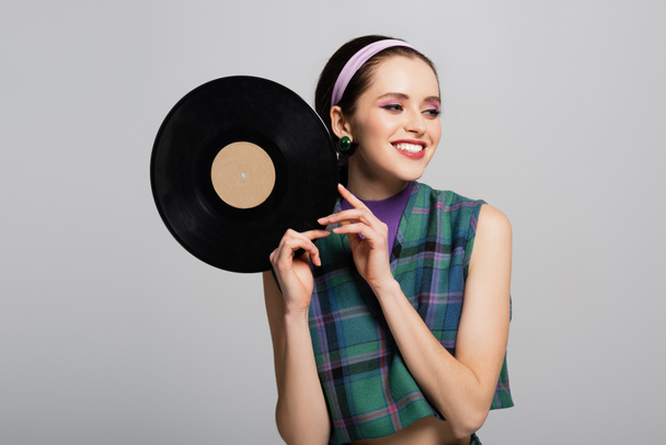 cheerful woman in headband holding retro vinyl disc isolated on grey - Zdjęcie, obraz