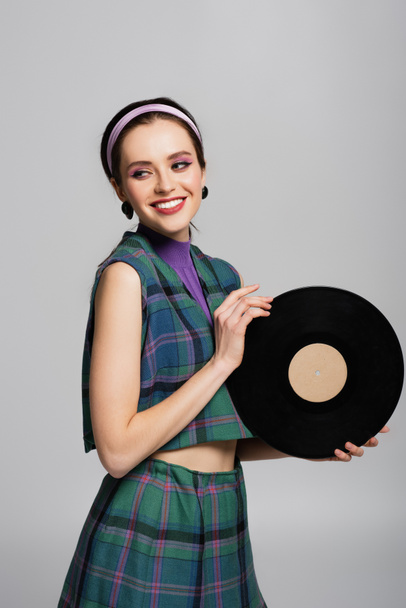 šťastná mladá žena v čelence drží retro vinylový disk izolované na šedé - Fotografie, Obrázek