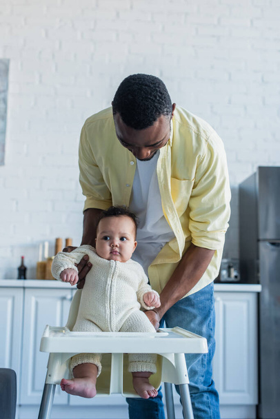 africano americano hombre holding bebé niño cerca de silla de bebé - Foto, Imagen