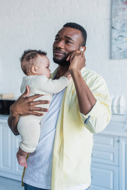 smiling african american man holding infant child while calling on smartphone - Photo, Image