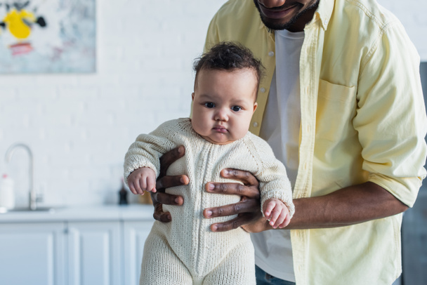 infant child in knitted romper in hands of african american father - Фото, изображение