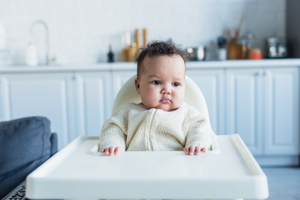 Afrikaans amerikaans kind meisje zitten in baby stoel in keuken - Foto, afbeelding