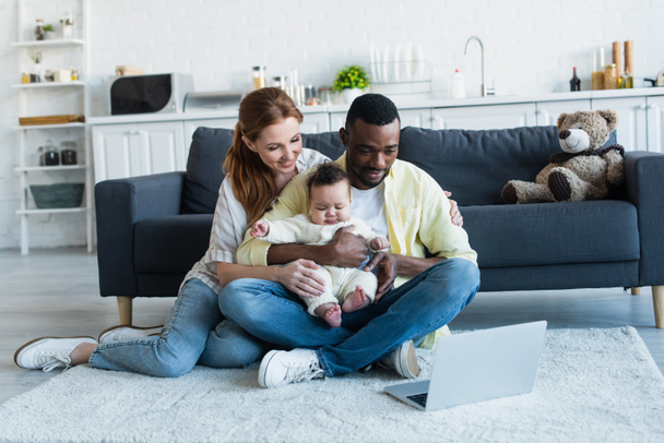multicultural parents with baby girl watching movie on laptop on floor - Photo, Image