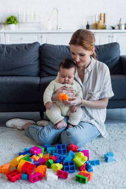woman sitting on floor with infant african american girl near multicolored building blocks - Photo, image