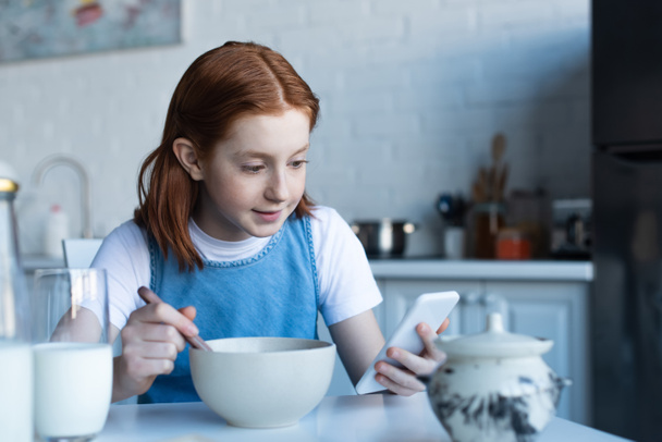 pelirroja chica usando smartphone mientras desayuna - Foto, Imagen