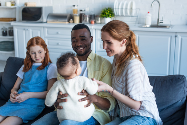 happy african american man holding infant child near smiling multiethnic family - Фото, изображение