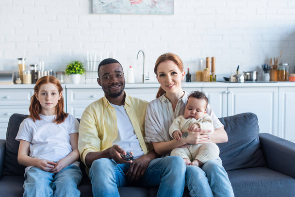 vreugdevolle Afrikaanse Amerikaanse man klikken kanalen terwijl het kijken van tv met multi-etnische familie - Foto, afbeelding
