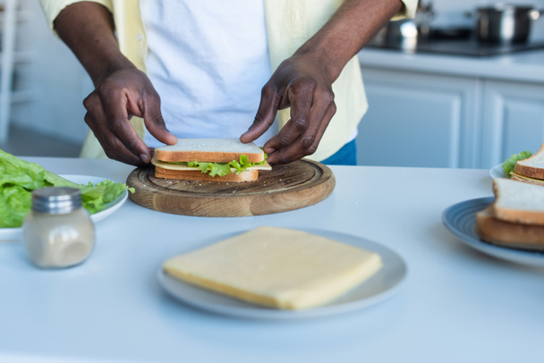 Teilansicht eines afrikanisch-amerikanischen Mannes, der Sandwich zum Frühstück macht - Foto, Bild