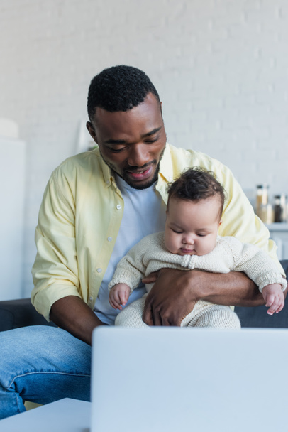 african american man holding baby girl near blurred laptop - Foto, Imagem