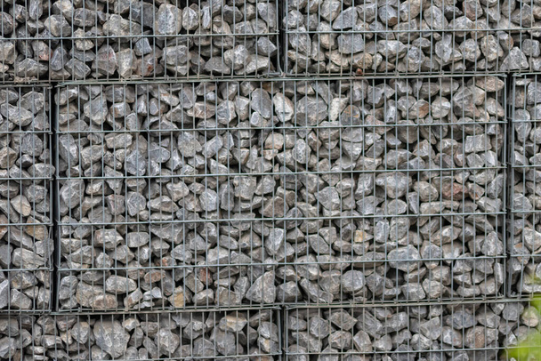 Protective gabions with grey broken stones behind grid as solid fence and solid wall and decorative element in gardens with rough surface textured as rock background and natural modern architecture - Foto, Imagem