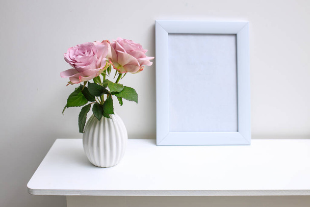 Egy halvány lila rózsa fehér furulyás vázában és képkeretben, szöveggel az asztalon díszítésként az esküvői fogadáshoz. - Fotó, kép