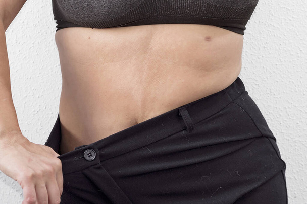 Жінка в процесі втрати ваги показує великі штани
 - Фото, зображення