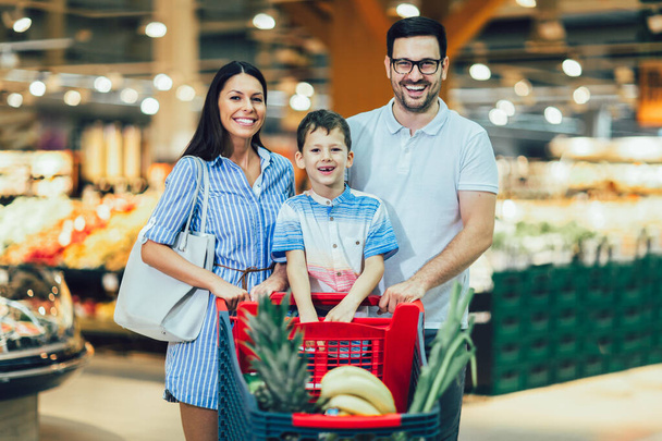 Ευτυχισμένη οικογένεια με παιδί και καλάθι αγορών που αγοράζουν τρόφιμα σε παντοπωλείο ή σούπερ μάρκετ - Φωτογραφία, εικόνα