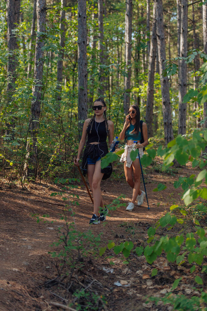 Sisters hiking through beautiful woods while wearing a backpack and enjoying nature. Female bonding. - Fotografie, Obrázek
