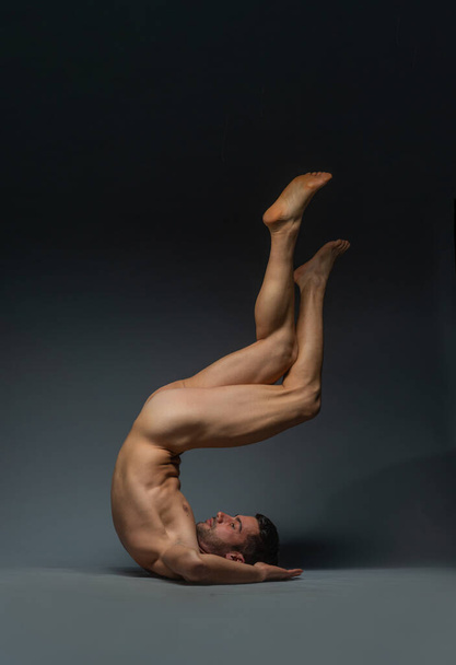 Karanlık bir stüdyoda bacakları havada yerde yatan çıplak bir genç adamın baş aşağı fotoğrafı. - Fotoğraf, Görsel