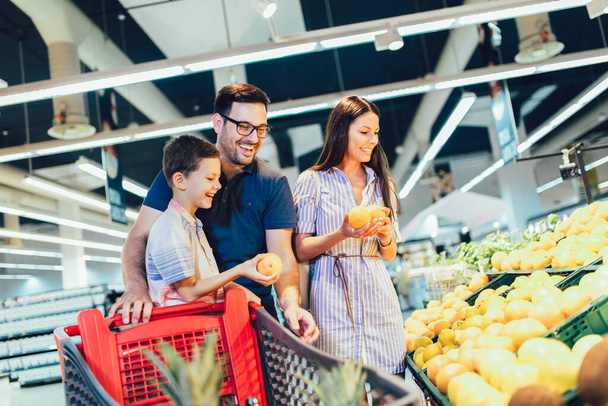 Ευτυχισμένη οικογένεια που αγοράζει φρούτα στο μπακάλικο ή στο σούπερ μάρκετ - ψώνια, φαγητό, πώληση, καταναλωτισμός - Φωτογραφία, εικόνα