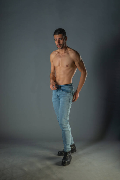 Full body portrait of sports man with denim jeans posing with bare torso in a dark studio - Фото, изображение