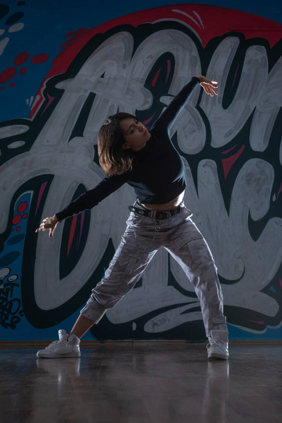 Silueta mladé hiphopové tanečnice (breakdancer) tančící na pozadí graffiti studia. Kontrastní barvy. - Fotografie, Obrázek