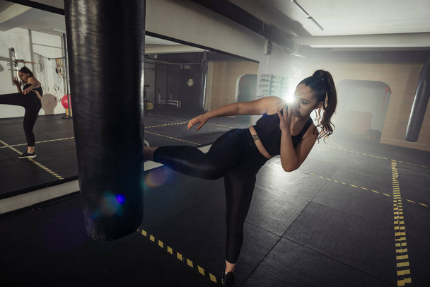 Νεαρή ενήλικη σέξι γυναίκα κάνει πίσω πόδι υψηλή κλωτσιά κατά τη διάρκεια kickboxing. - Φωτογραφία, εικόνα