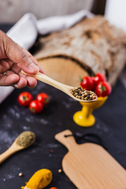 A hand holding a wooden spoon with spices and cherry tomatoes on the table - Foto, immagini