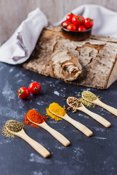The wooden spoons with spices, paprika, basilic, pepper, thyme with cherry tomatoes - Photo, Image