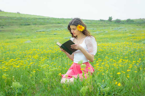 красивая молодая женщина в поле читает книгу, женщина читает книгу, девушка в поле с цветами - Фото, изображение