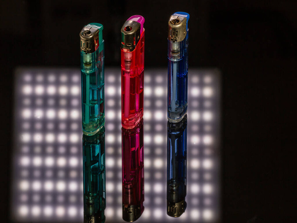 Three gas lighters in different colours on a black reflecting background with white light reflections - Foto, Imagem