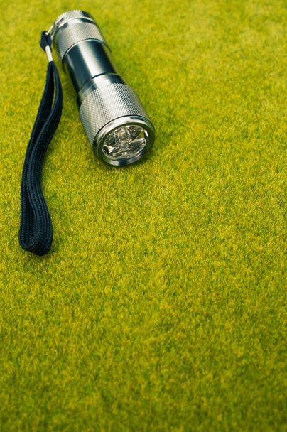 A grey and black flashlight on a green grass surface - Zdjęcie, obraz