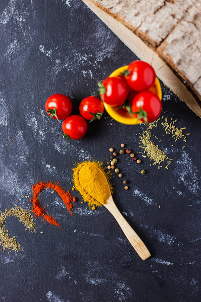 A spoon and spices with cherry tomatoes on a dark table - Fotografie, Obrázek