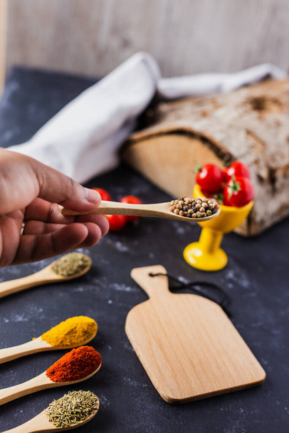 A hand holding a wooden spoon with spices and cherry tomatoes on the table - 写真・画像