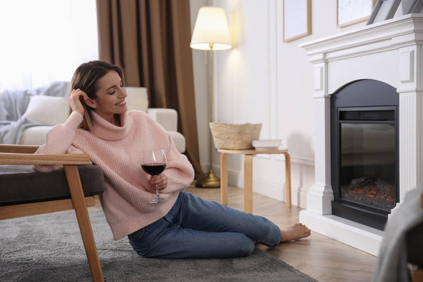 Young woman with glass of wine resting near fireplace at home - Foto, Bild
