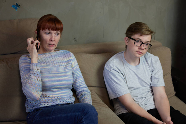 High resolution photo mother talking on phone next to indifferent son at home - 写真・画像