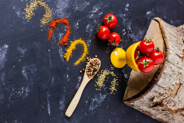 A spoon and spices with cherry tomatoes on a dark table - Photo, Image
