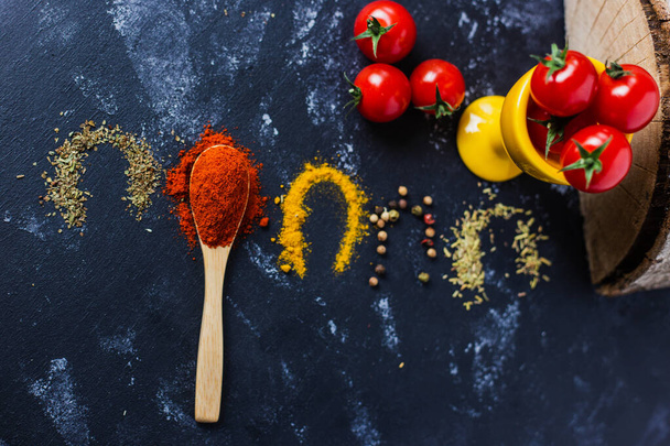 A spoon and spices with cherry tomatoes on a dark table - 写真・画像