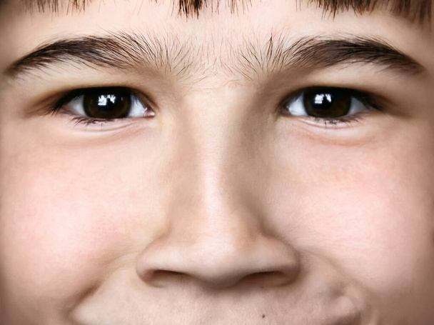 eine lustige Nahaufnahme eines braunäugigen lächelnden Jungen, der Fratzen, Mimik, Nasenfalten und geschwollene Nasenlöcher macht; Blick direkt in die Kameralinse, waagerecht - Foto, Bild
