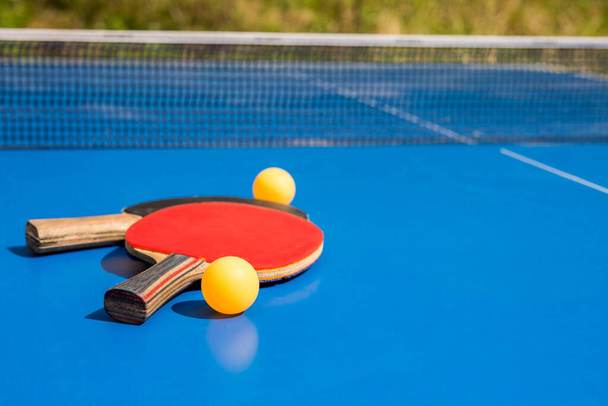  Tafeltennis buiten. Een close-up pingpong. Accessoires voor tafeltennisracket en bal op een blauwe tennistafel. Sport. - Foto, afbeelding
