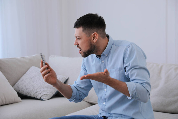Emotional man with smartphone at home. Online hate concept - Photo, image