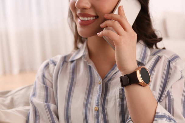 Young woman with smart watch talking on phone at home, closeup - Фото, изображение