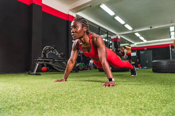sterke atletische zwarte vrouw in een sportschool doen push-up oefeningen in rode sportkleding - Foto, afbeelding