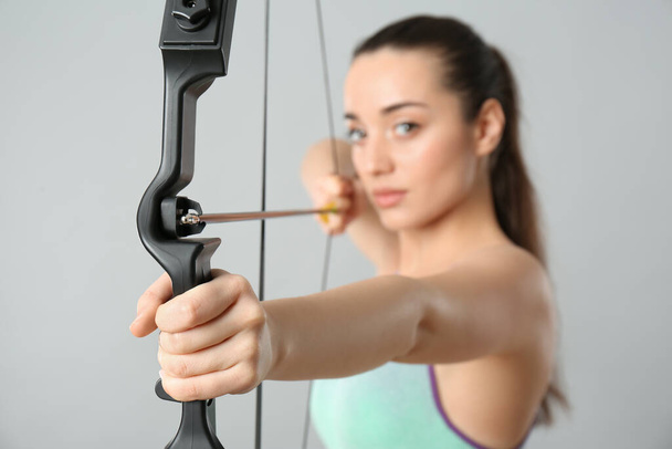 Young woman practicing archery against light grey background, focus on bow - Foto, immagini