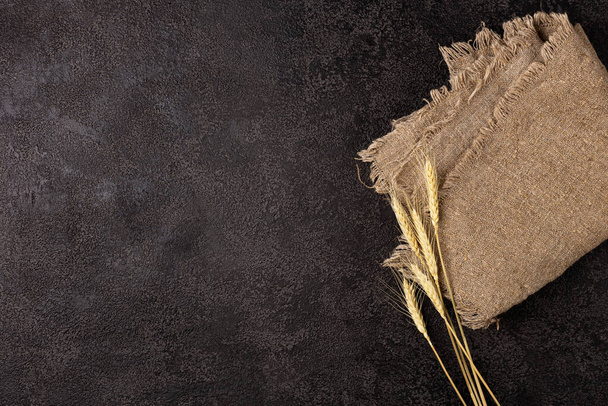 Burlap napkin on a dark structural background, top view. Ears of wheat. Copyspace - Фото, изображение